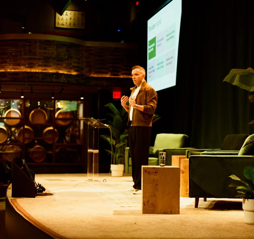 Speaker presenting on stage beside green lounge chairs at an AirOps event
